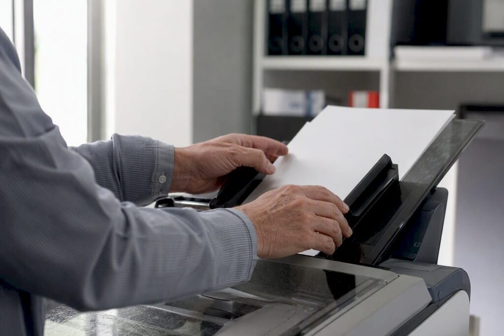 Mãos colocando documentos no scanner para digitalização